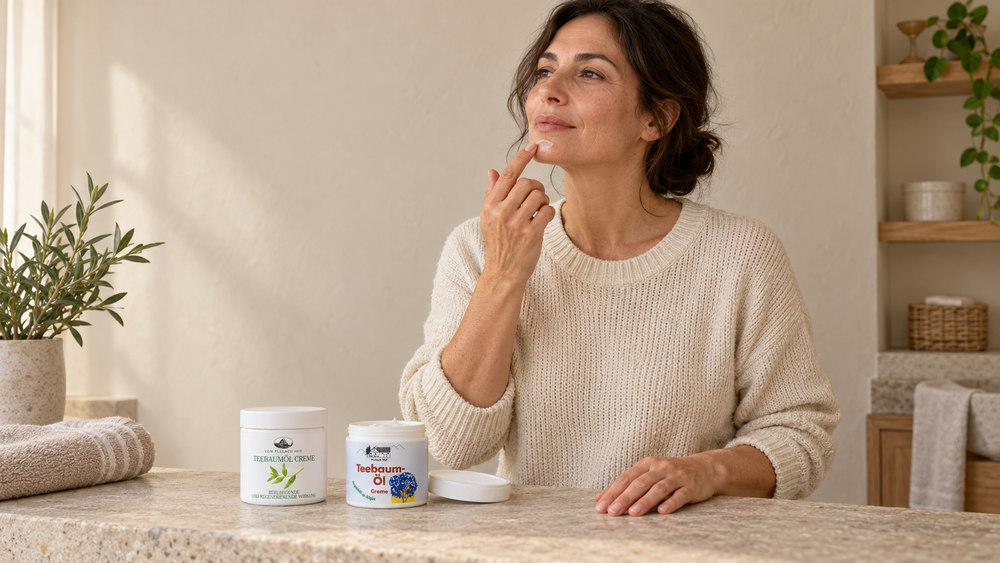 Donna in bagno che applica con il dito un po’ di crema tea tree sul mento, con due vasetti aperti sul piano