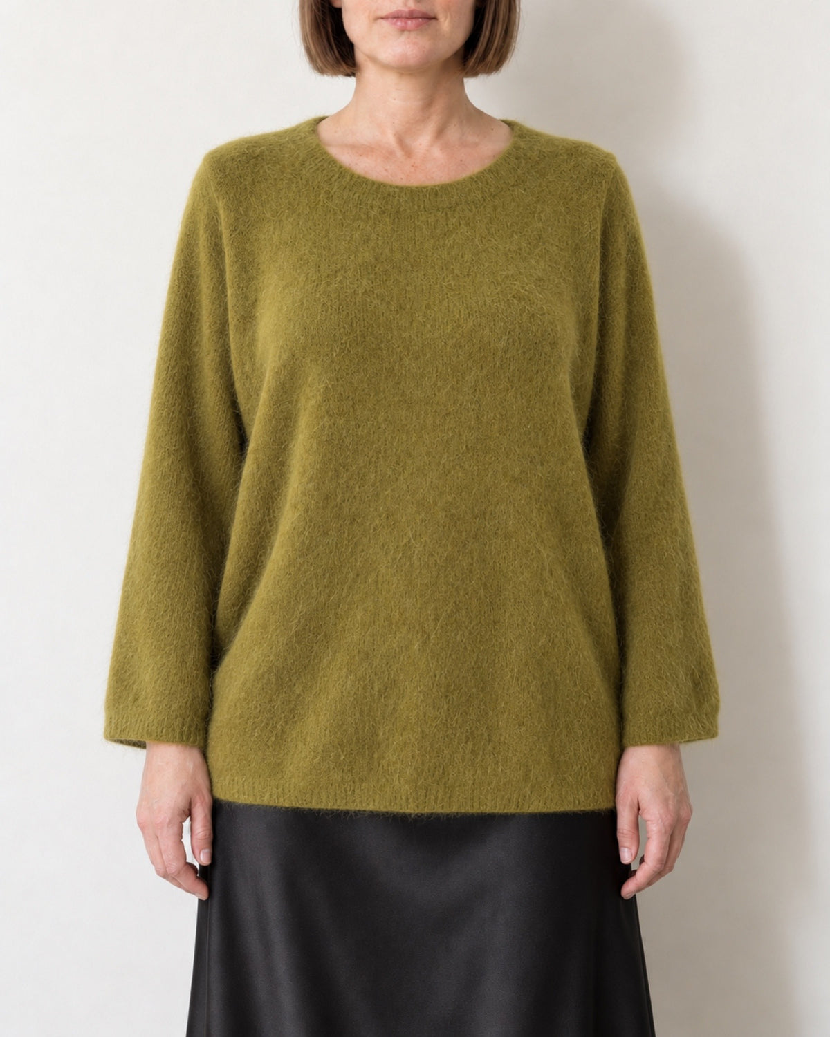 Maglione oversize verde oliva indossato con gonna nera in raso, vista frontale