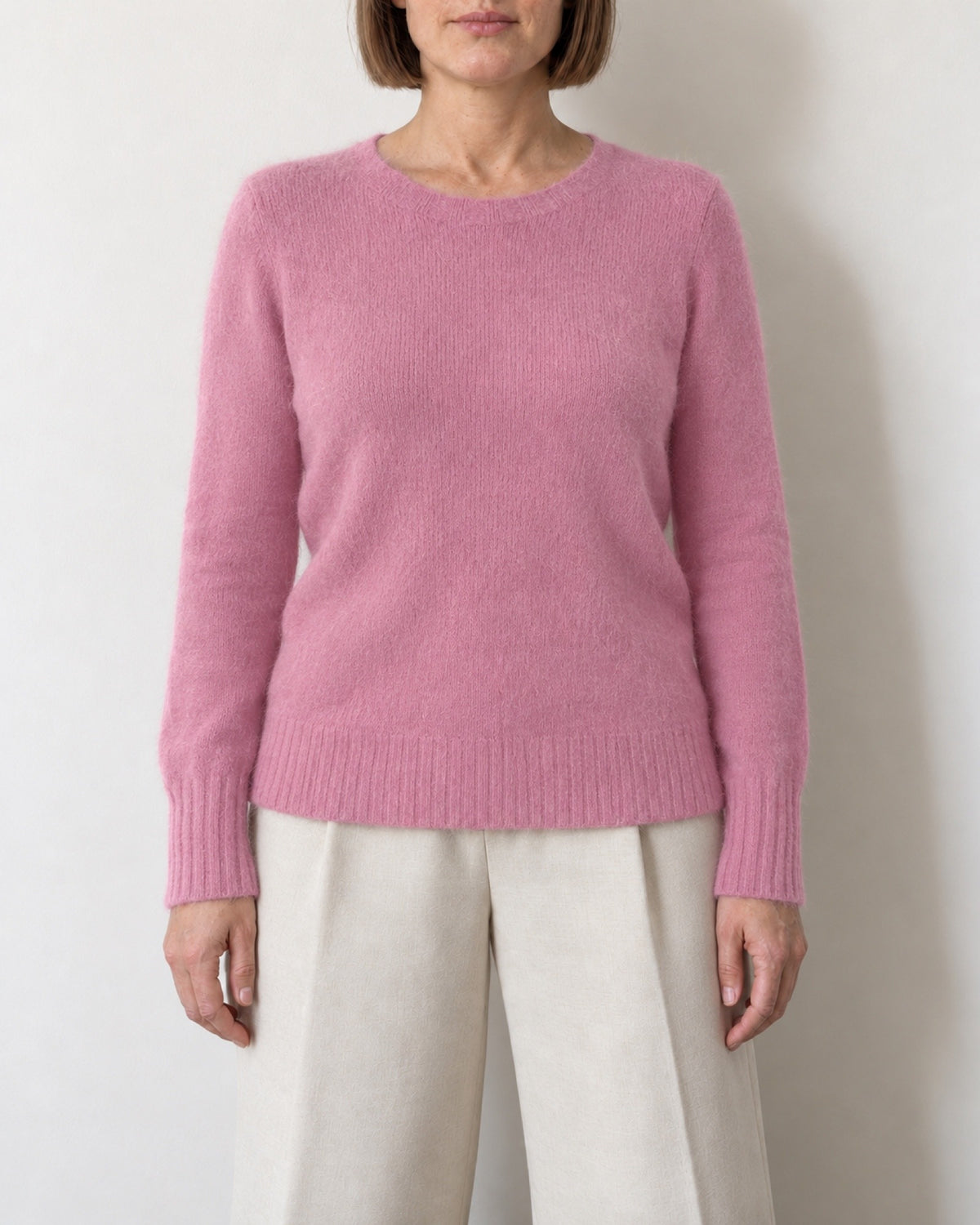Maglione girocollo rosa aderente indossato con pantaloni ecru, vista frontale