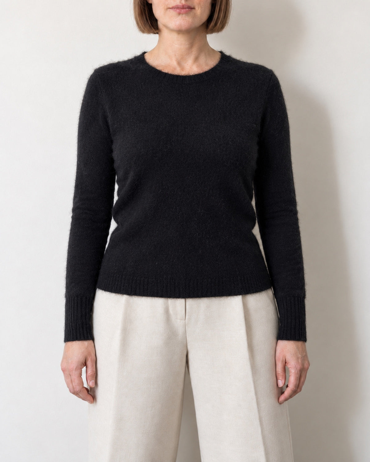 Maglione girocollo nero aderente indossato con pantaloni ecru, vista frontale