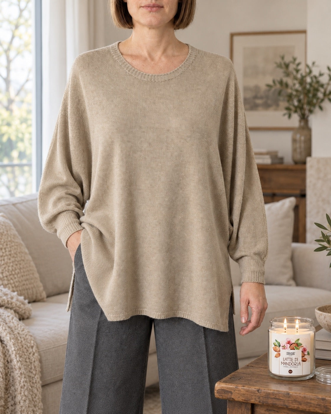 Maglione oversize beige con maniche a pipistrello indossato con pantaloni grigi in salotto